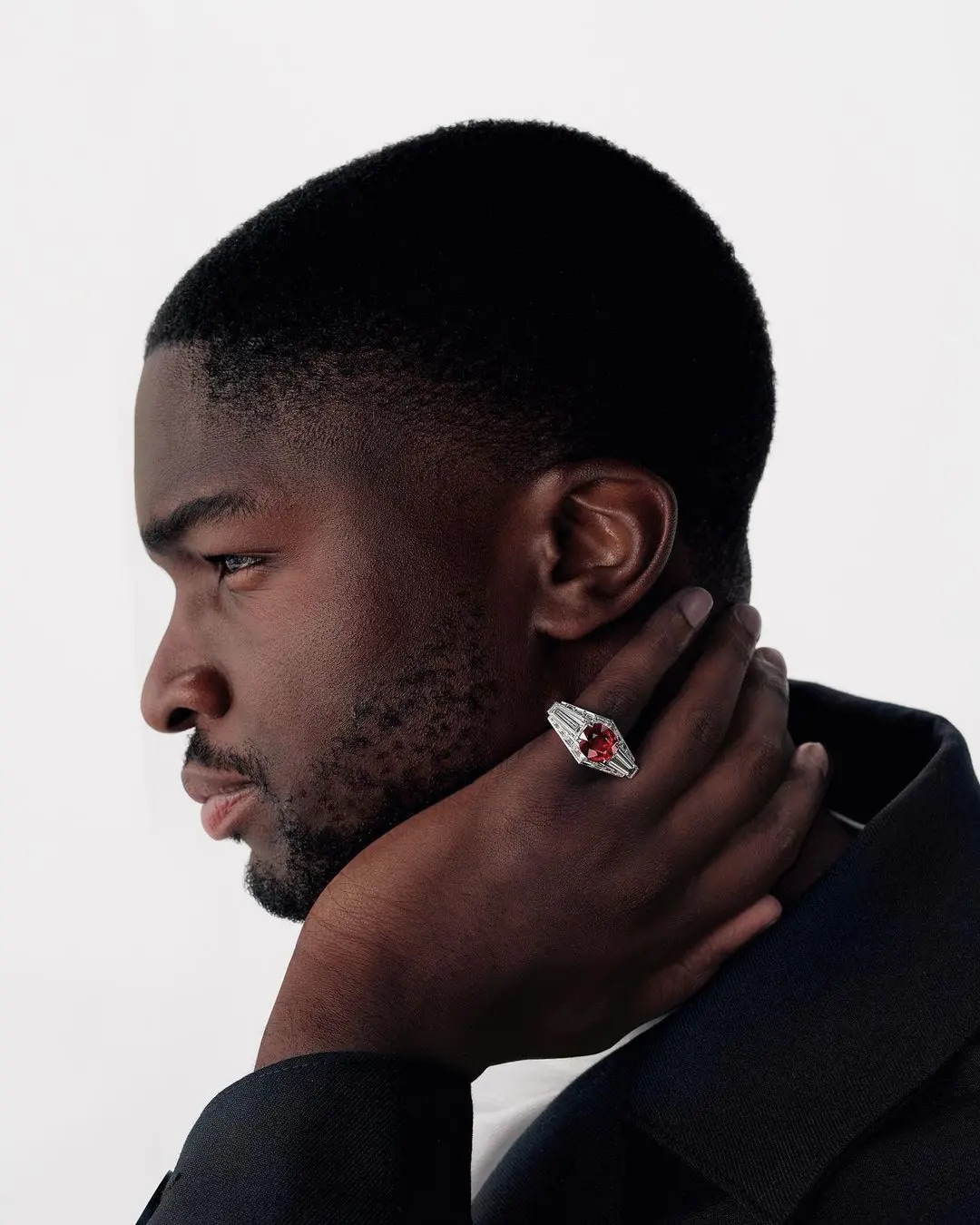 A man in black clothes wearing a ring with diamonds and a red gemstone